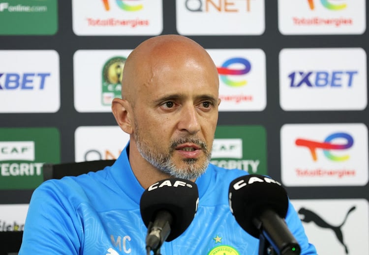 Miguel Cardoso speaking at a press conference with CAF-branded microphones in front of him.