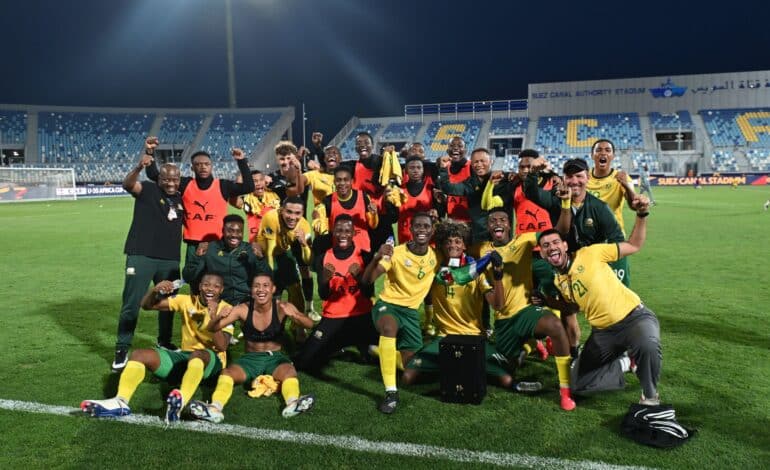 Amajita players and staff celebrating on the pitch with raised arms and wide smiles.